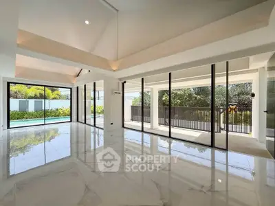 Spacious modern living room with floor-to-ceiling windows and pool view, featuring elegant marble flooring.