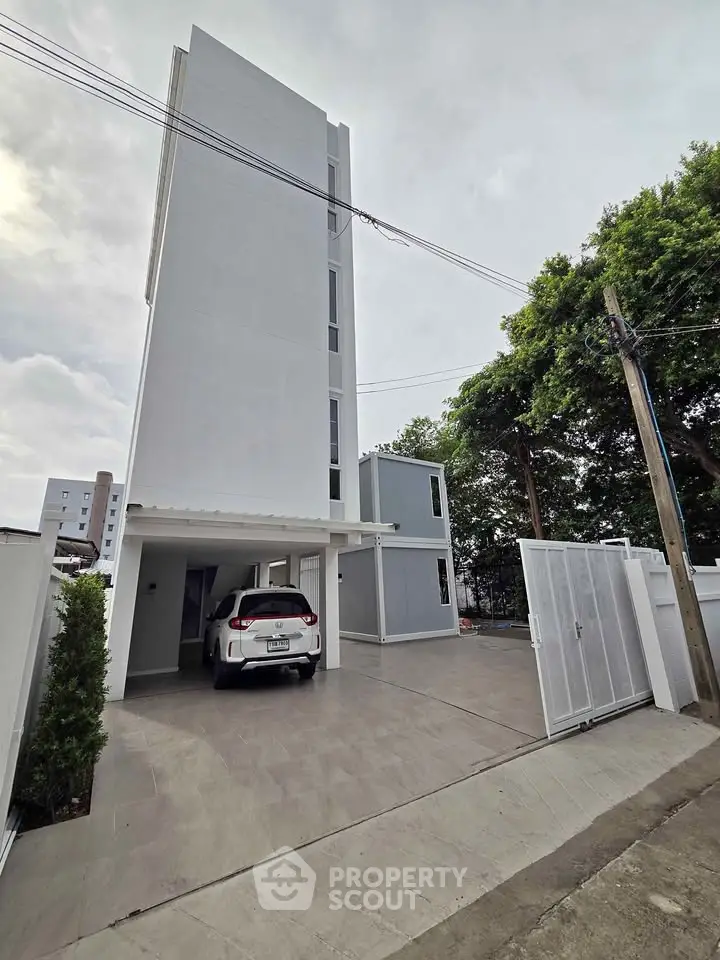 Modern multi-story building with parking space and gated entrance, surrounded by greenery.