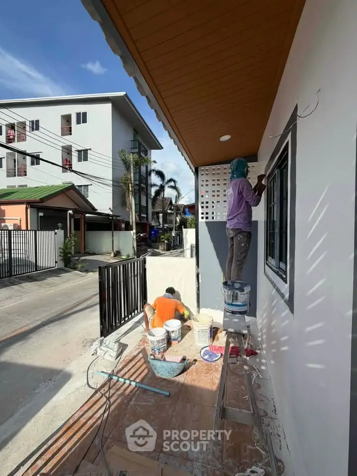 Exterior home renovation with workers painting and repairing facade in residential neighborhood.