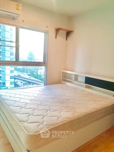 Bright bedroom with large window and city view, featuring a comfortable bed and wooden flooring.