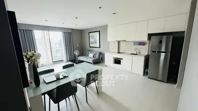 Modern open-layout living room with kitchen and dining area, featuring sleek furniture and natural light.