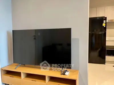Modern living room with sleek TV and stylish wooden cabinet, adjacent to a contemporary kitchen.