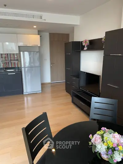 Modern living room with sleek black furniture and open kitchen layout, featuring a stylish dining area and vibrant decor.