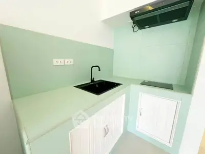 Modern compact kitchen with mint green cabinets and black sink, featuring a sleek stovetop and extractor fan.