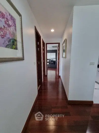 Elegant hallway with wooden flooring and framed artwork leading to a modern interior space.
