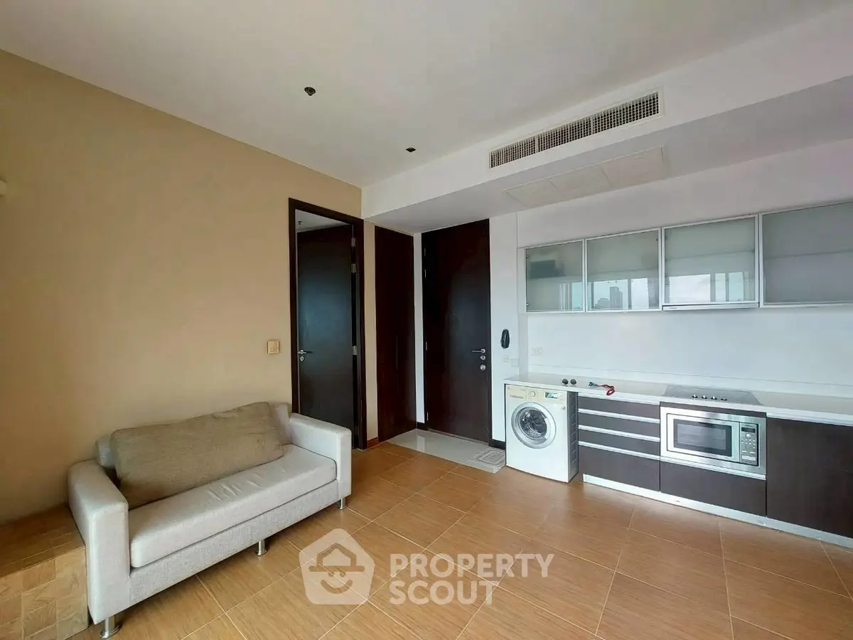 Modern living room with integrated kitchen featuring washing machine and microwave.