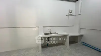 Minimalist kitchen with white countertops and sink, featuring a simple design and tiled flooring.