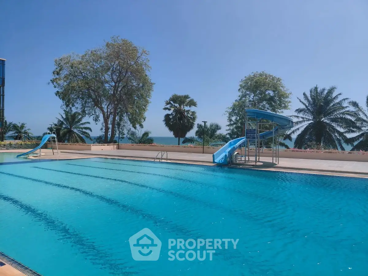 Luxurious outdoor pool with slides and ocean view, surrounded by tropical trees.