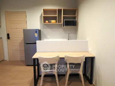 Modern kitchen with fridge, microwave, and dining area in compact apartment.