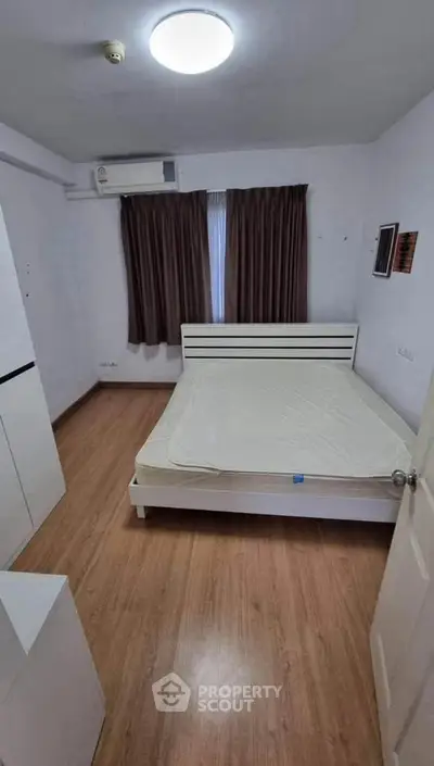 Cozy bedroom with wooden flooring and natural light, featuring a minimalist bed and air conditioning.