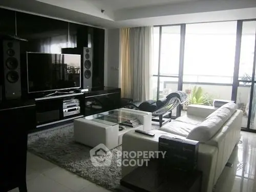 Modern living room with sleek furniture and large TV, featuring floor-to-ceiling windows and balcony access.