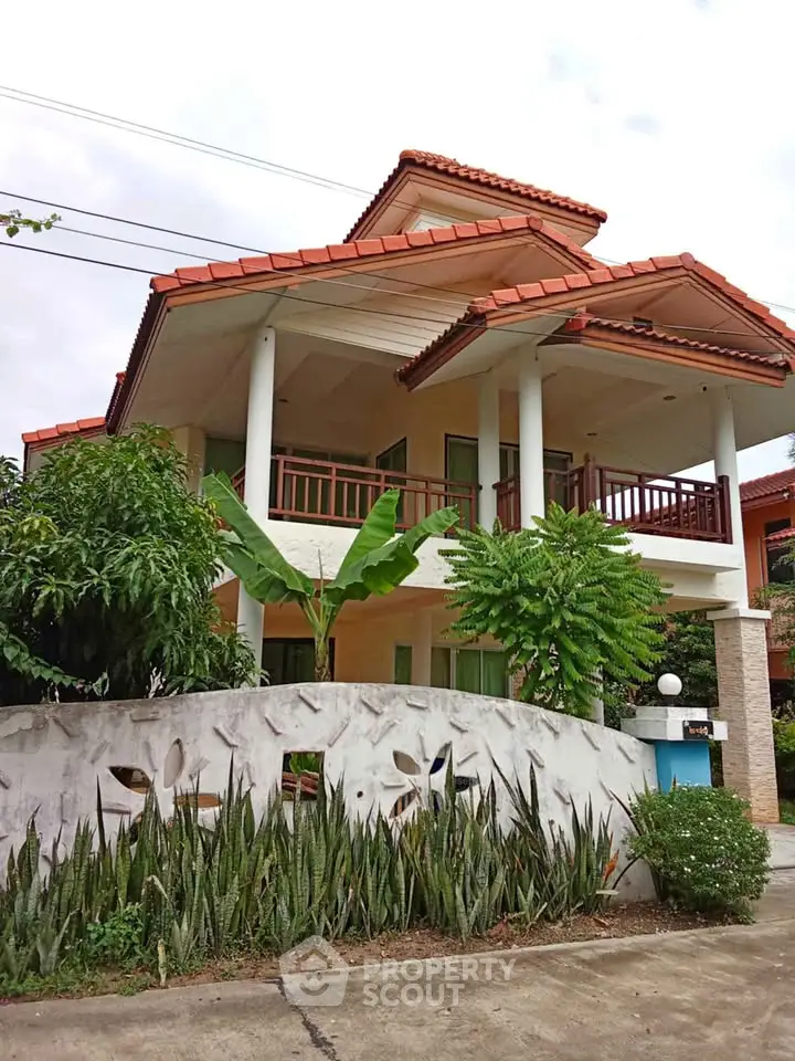 Charming two-story house with red-tiled roof and lush garden, perfect for family living.