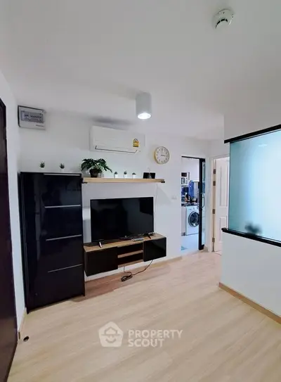 Modern living room with sleek TV unit and air conditioning, adjacent to a visible kitchen area.