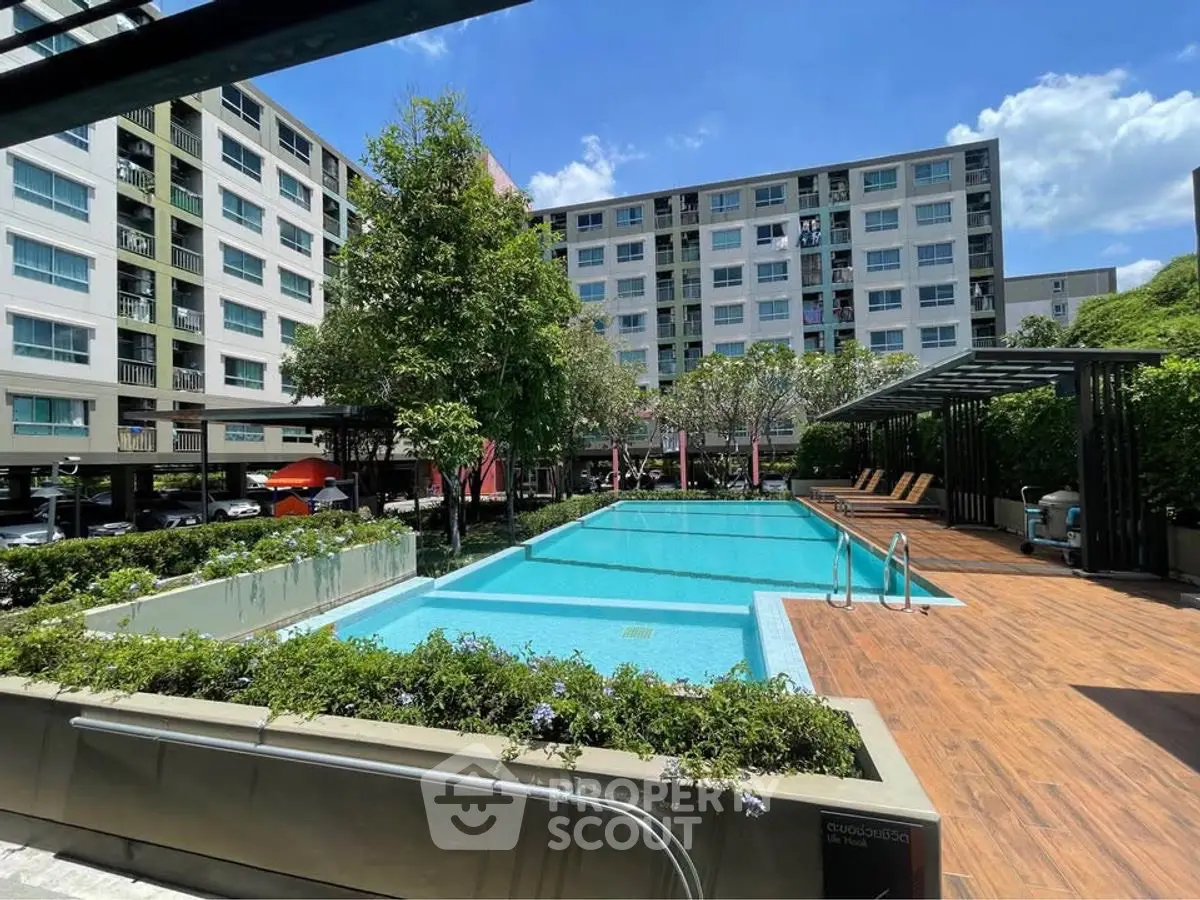 Modern apartment complex with a pristine swimming pool and lush greenery under a clear blue sky.