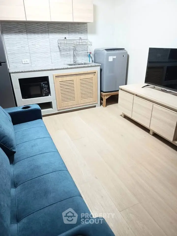 Modern living room with compact kitchen and stylish blue sofa, perfect for cozy urban living.