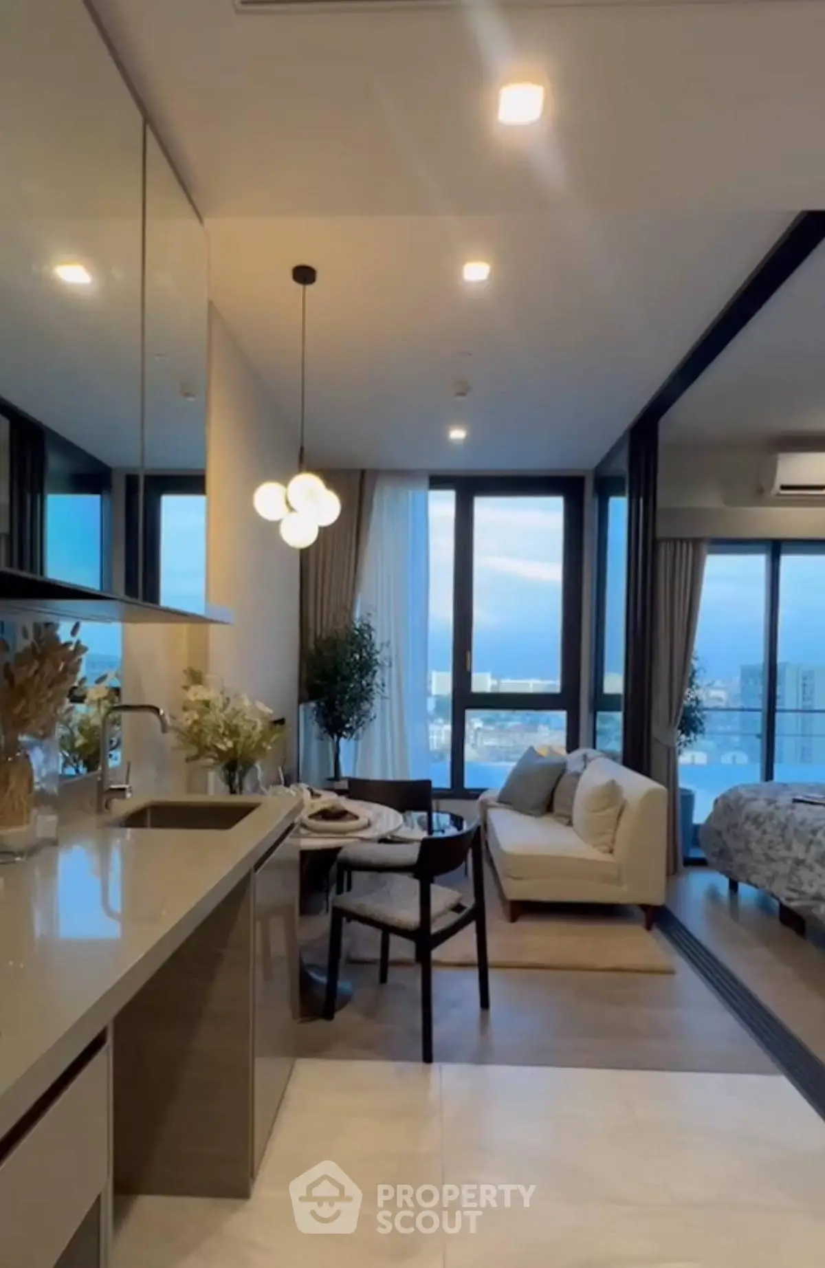 Modern open-plan living room with kitchen, featuring large windows and stylish decor.