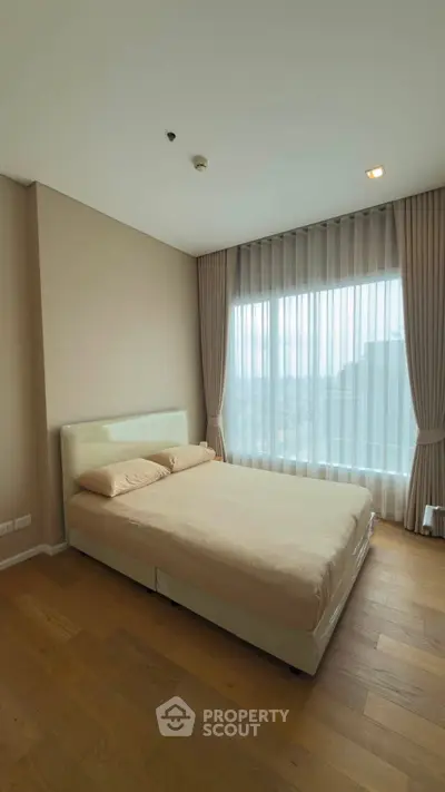 Spacious bedroom with large window and elegant curtains in modern apartment.