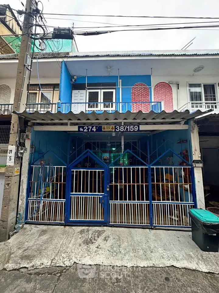 Charming two-story townhouse with colorful facade and gated entrance in urban setting.