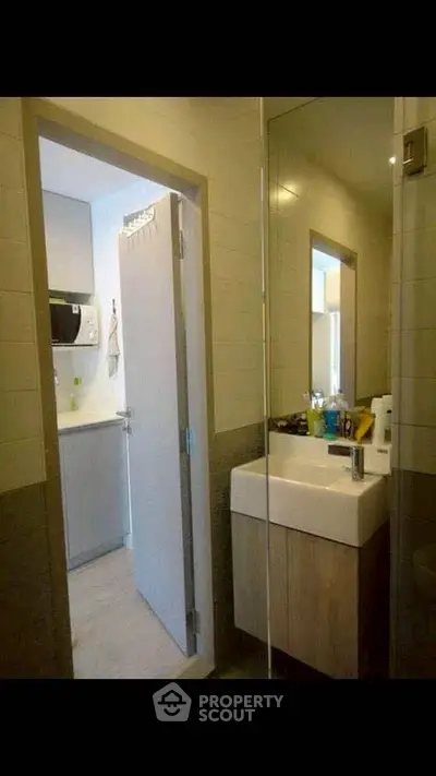 Modern bathroom with sleek sink and mirror, adjacent to a compact kitchen area.