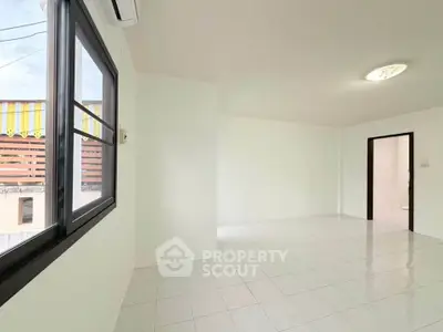 Spacious white-tiled room with large window and air conditioning, perfect for versatile living space.