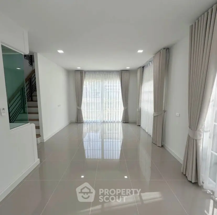 Spacious modern living room with large windows and elegant curtains, perfect for natural light.
