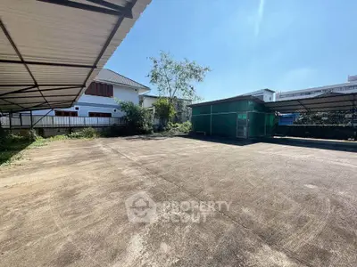 Spacious outdoor parking area with covered sections and nearby residential buildings.