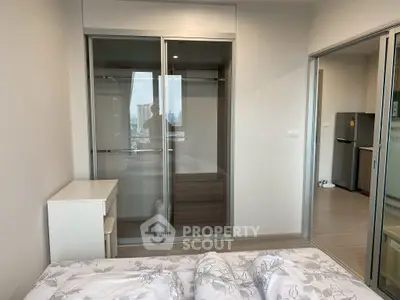 Modern bedroom with sliding glass closet doors and city view, featuring a compact workspace.