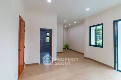 Spacious empty room with wooden flooring and large windows offering natural light
