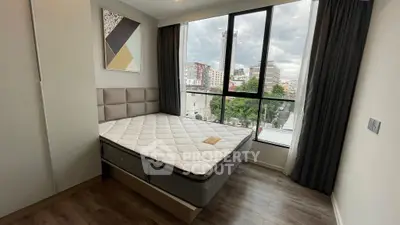 Modern bedroom with large window and city view, featuring stylish decor and comfortable mattress.