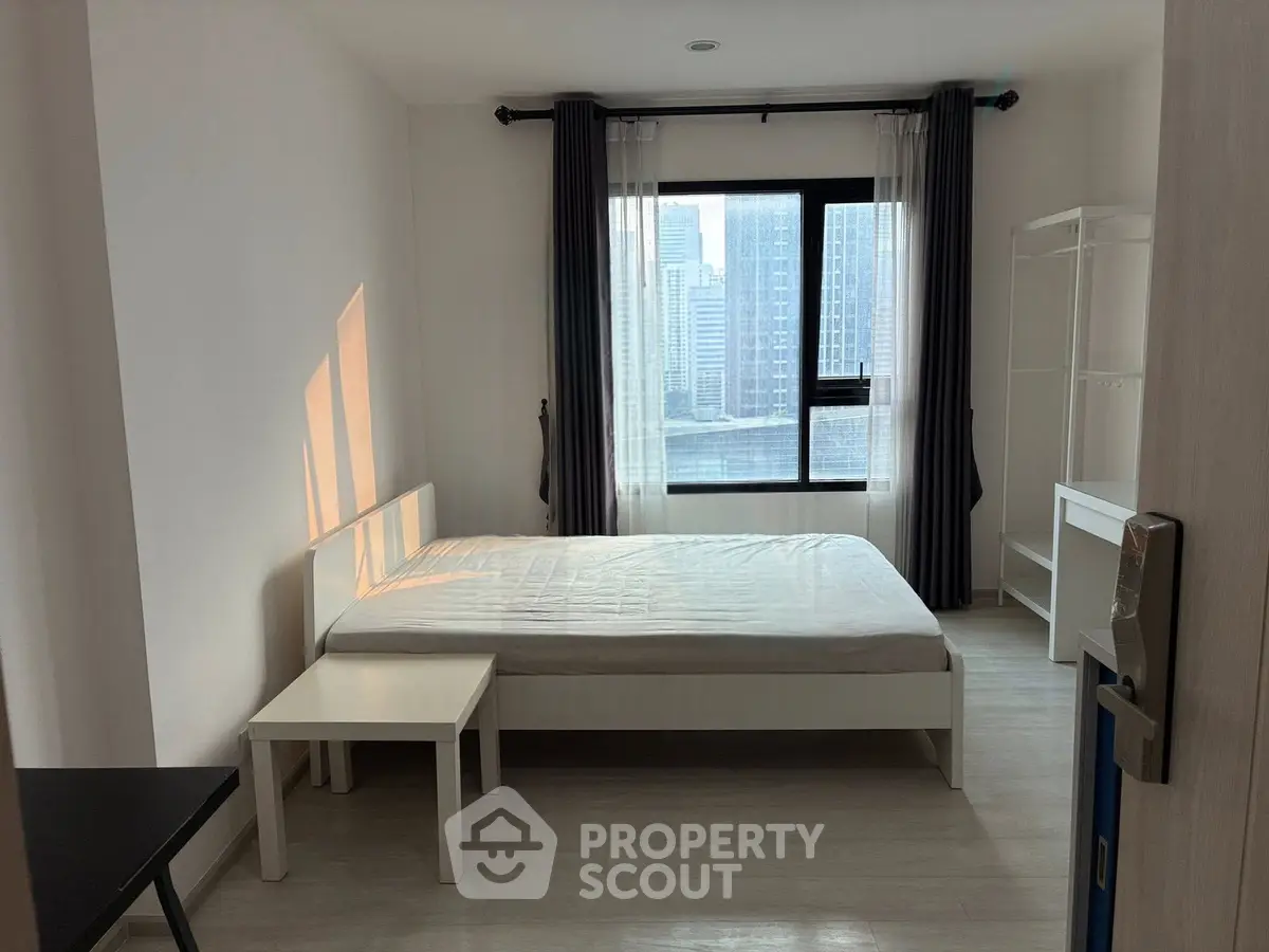 Modern bedroom with city view, featuring minimalist furniture and large window for natural light.