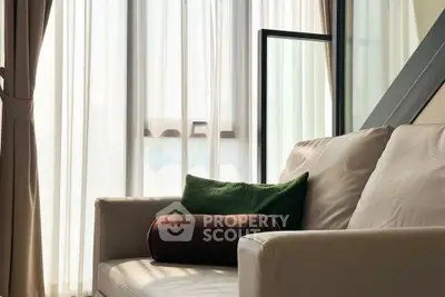 Cozy living room with elegant sofa and large window draped with sheer curtains, inviting natural light.