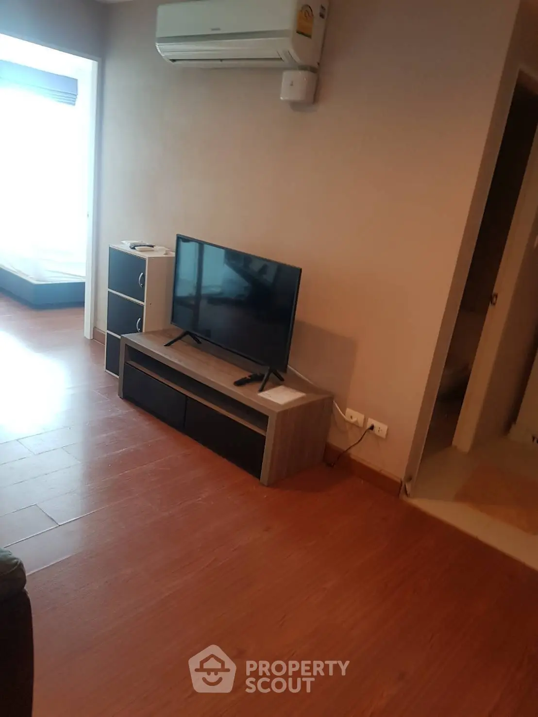 Modern living room with sleek TV stand and air conditioning, featuring wooden flooring and neutral walls.