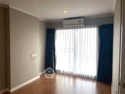 Spacious empty room with wooden flooring and large window with curtains