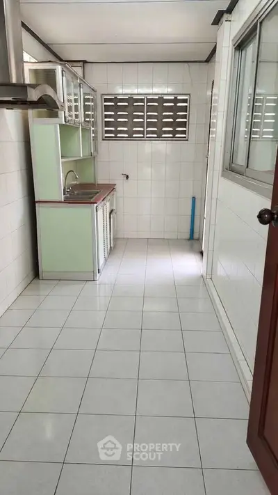 Spacious kitchen with tiled flooring and ample natural light, featuring a closed layout and modern cabinetry.