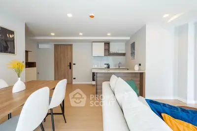 Modern open-plan living room with stylish kitchen and dining area, featuring sleek furniture and bright decor.