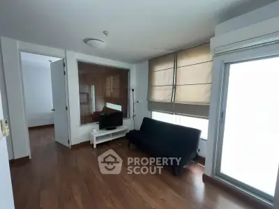 Modern living room with wooden flooring, large windows, and minimalist furniture.