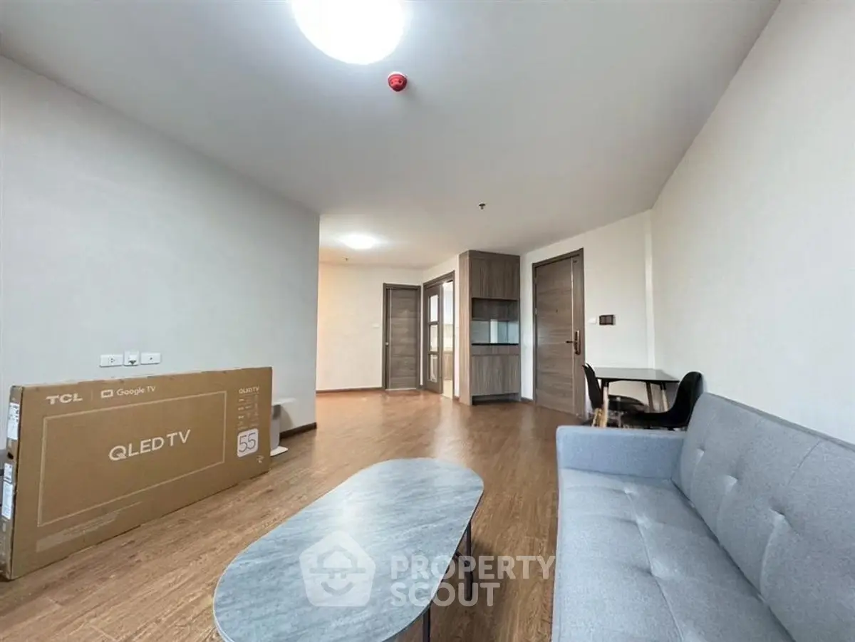Spacious living room with modern furniture and natural light, featuring a sleek grey sofa and a boxed QLED TV.