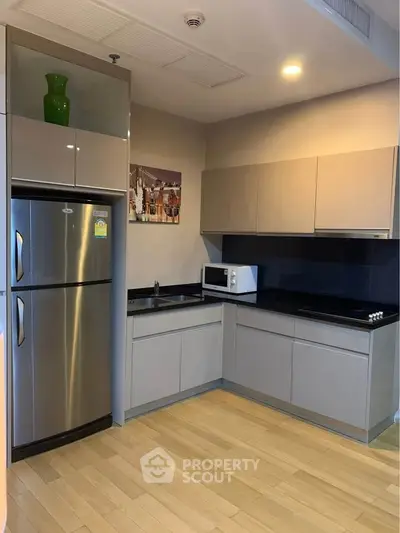 Modern kitchen with sleek cabinets, stainless steel fridge, and microwave in a compact layout.