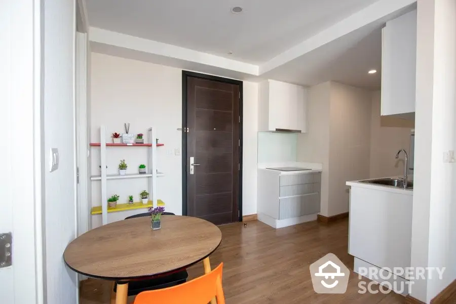 Modern apartment interior with compact kitchen and dining area, featuring sleek design and wooden flooring.