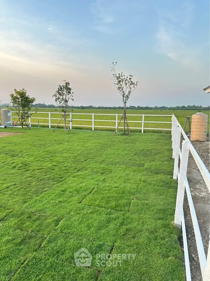 Expansive green lawn with white fence and scenic countryside view, perfect for outdoor activities.
