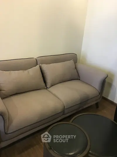 Cozy living room with modern beige sofa and round ottomans on wooden floor.