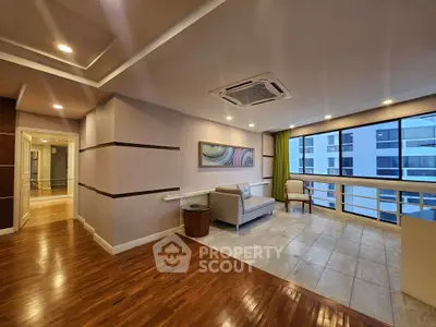 Spacious modern living room with hardwood floors and large windows offering city views.