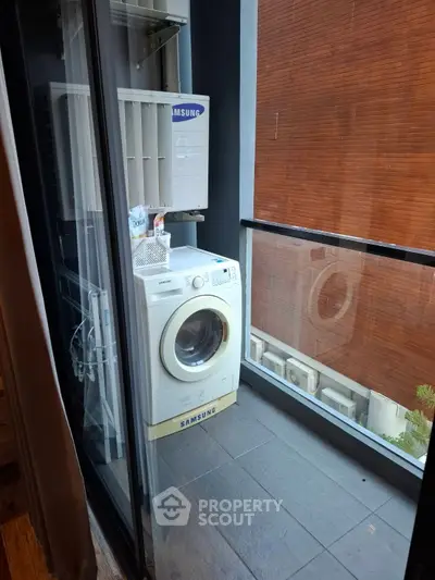 Modern balcony with washing machine and sleek glass railing in urban setting.