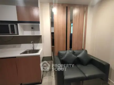 Modern compact living room with kitchenette featuring sleek cabinetry and cozy sofa.