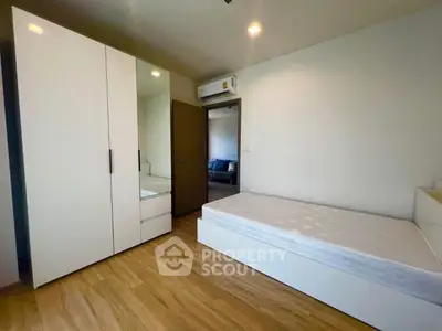 Modern minimalist bedroom with wooden flooring and sleek white furniture.
