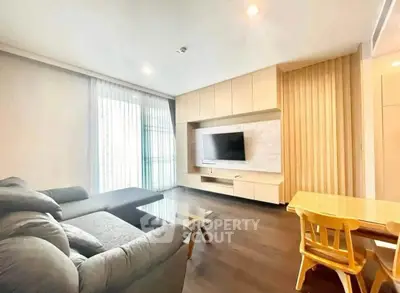 Modern living room with sleek furniture and large TV, featuring natural light and elegant design.