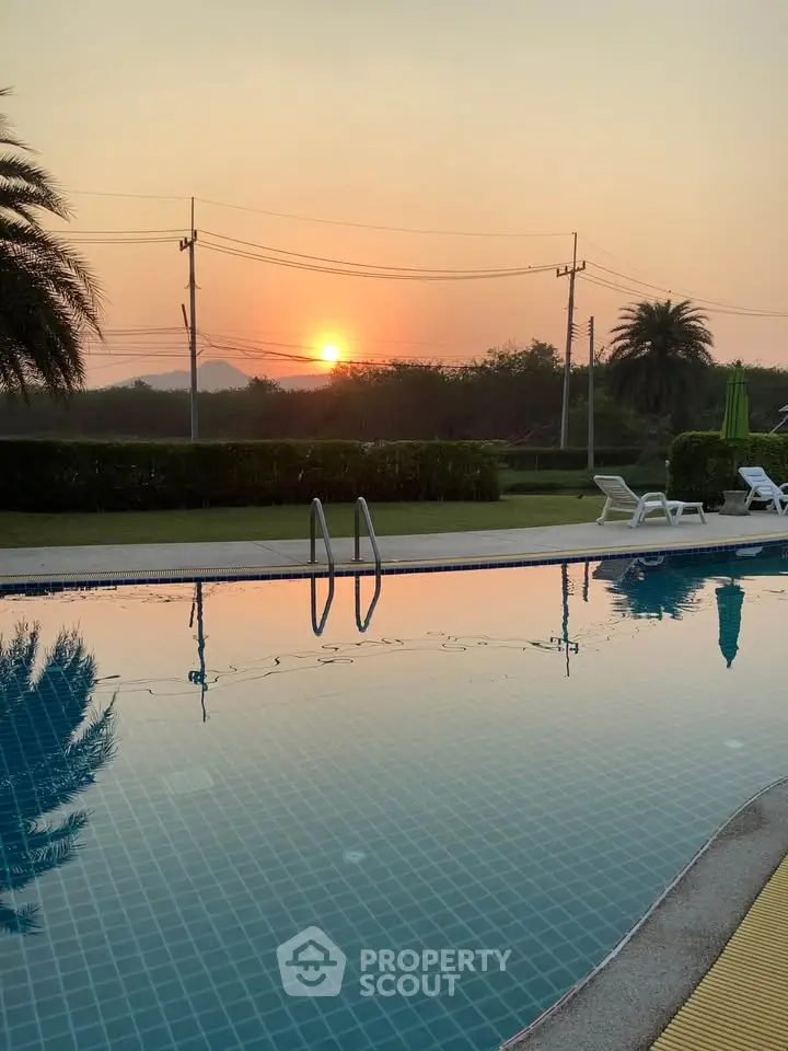 Stunning sunset view over a serene swimming pool with lush greenery, perfect for relaxation and leisure.