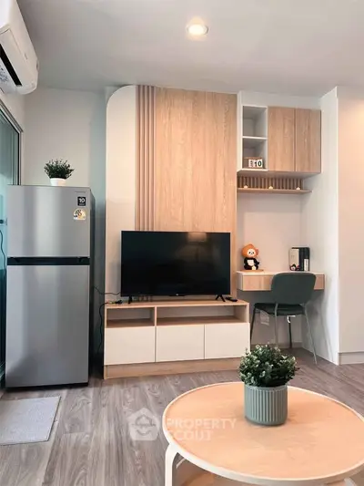 Modern living room with stylish decor, featuring a TV, fridge, and workspace in a cozy apartment.