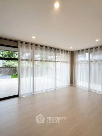 Spacious empty living room with large windows and elegant sheer curtains, offering a bright and airy atmosphere.