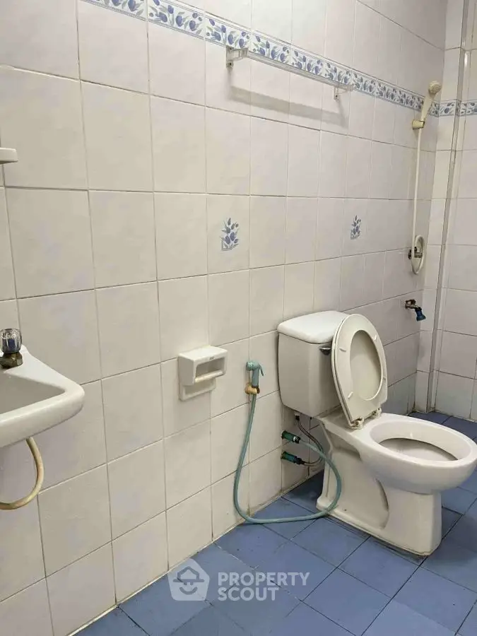 Spacious bathroom with white tiles and blue accents, featuring a toilet and sink.